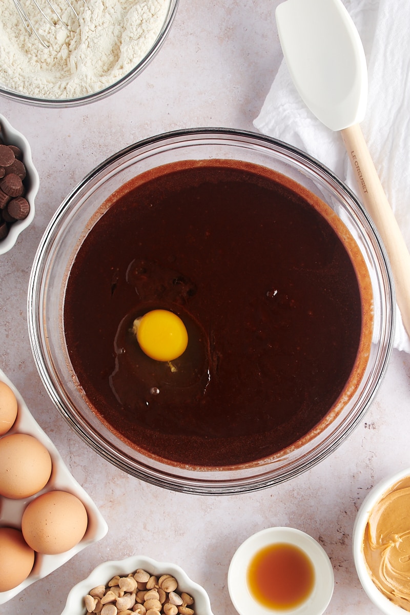 Overhead view of egg added to wet brownie ingredients