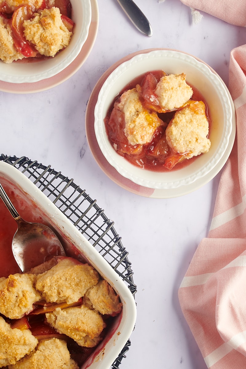 overhead view of plum cobbler in a white baking dish and served in white bowls