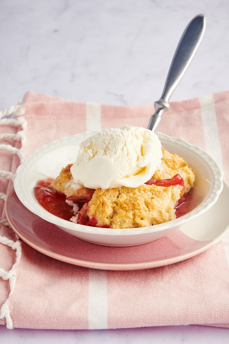 a serving of plum cobbler served in a white bowl and topped with ice cream