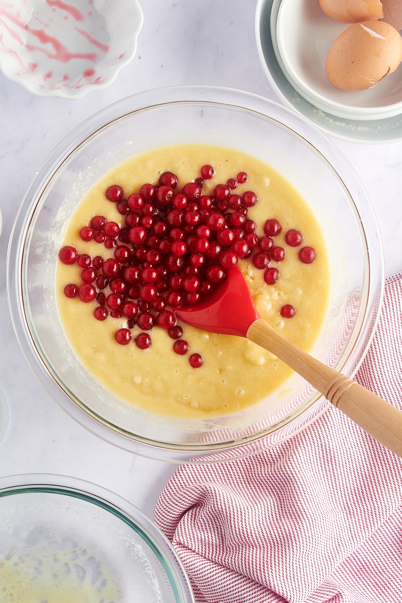 overhead view of red currants added to muffin batter in a glass mixing bowl