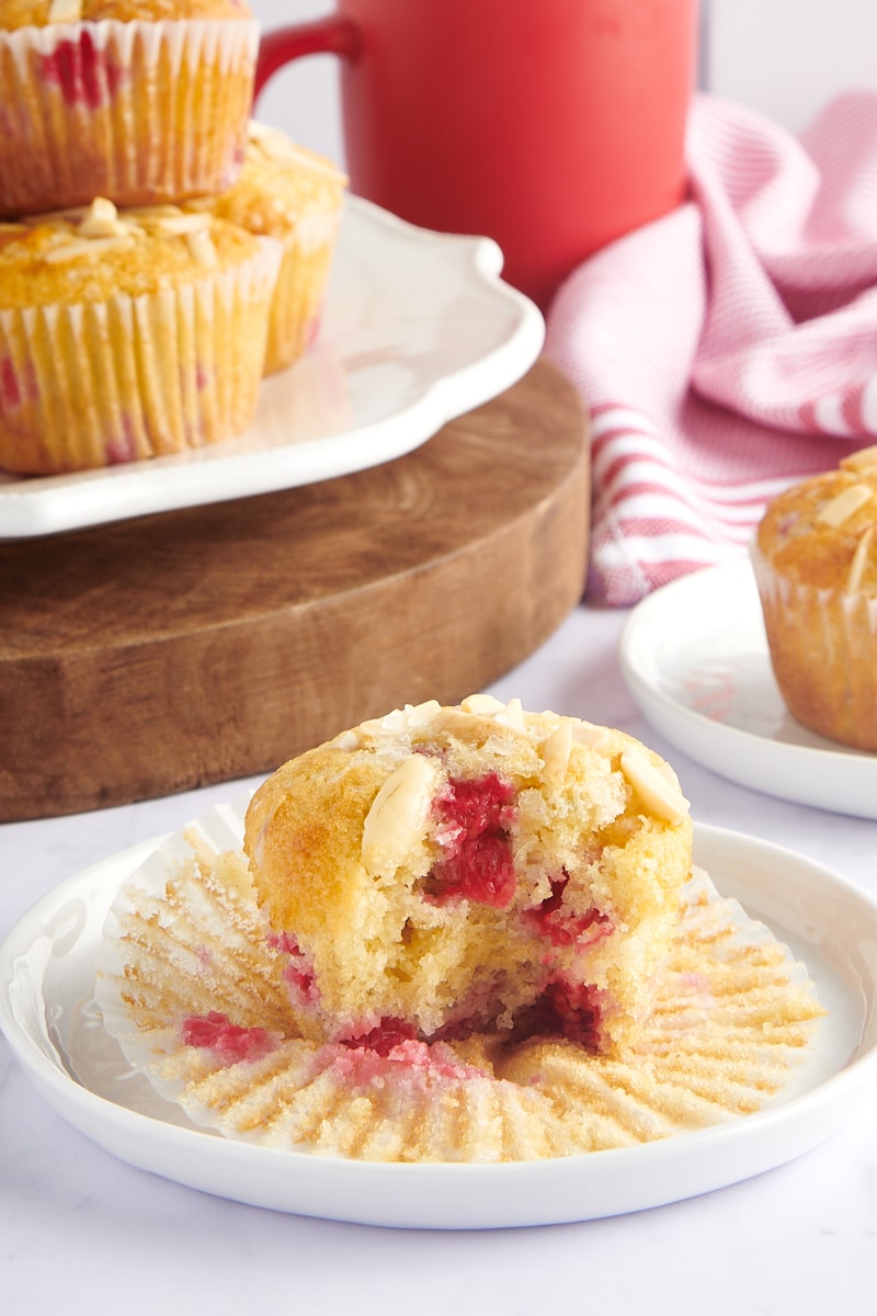 part of a Red Currant Muffin on a white plate with more muffins in the background