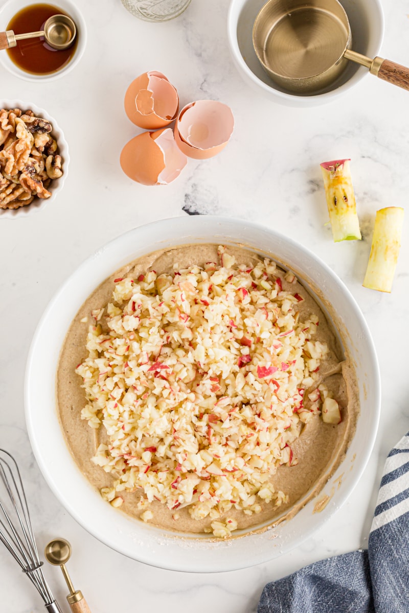 overhead view of apples added to cake batter in a white mixing bowl