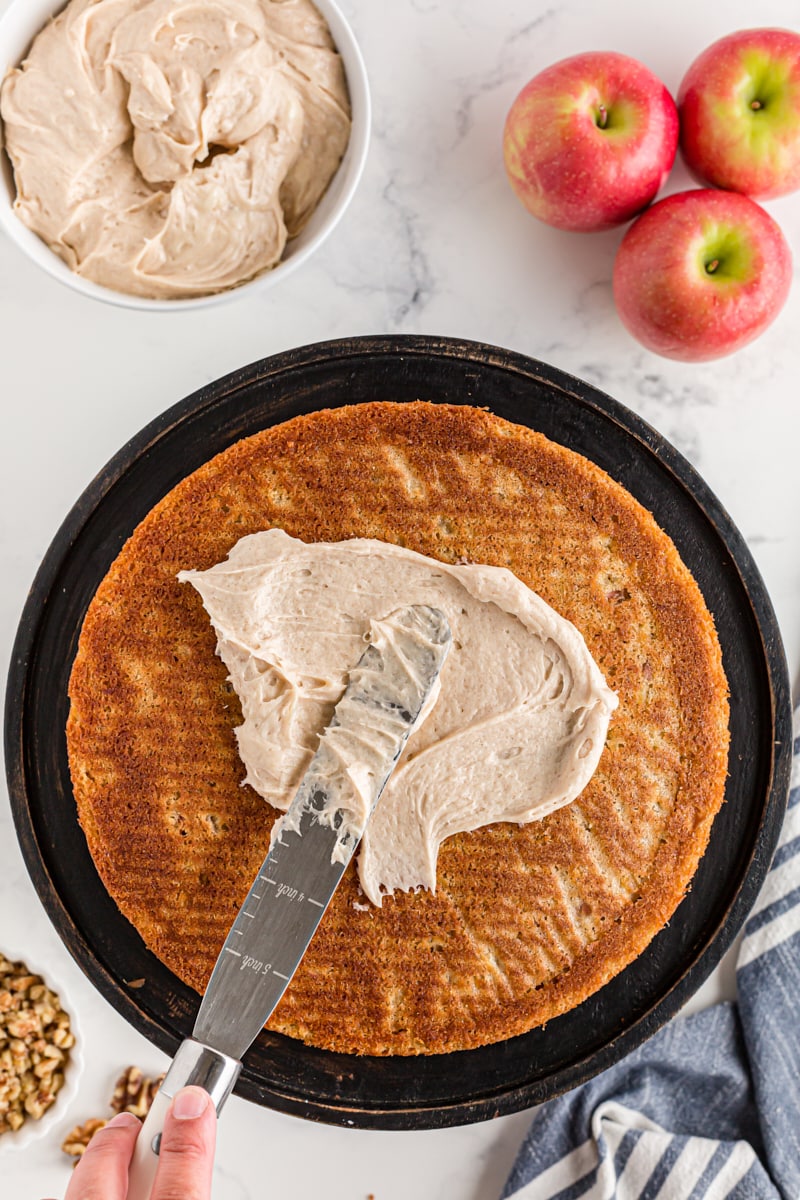 overhead view of frosting being spread onto an apple spice cake layer