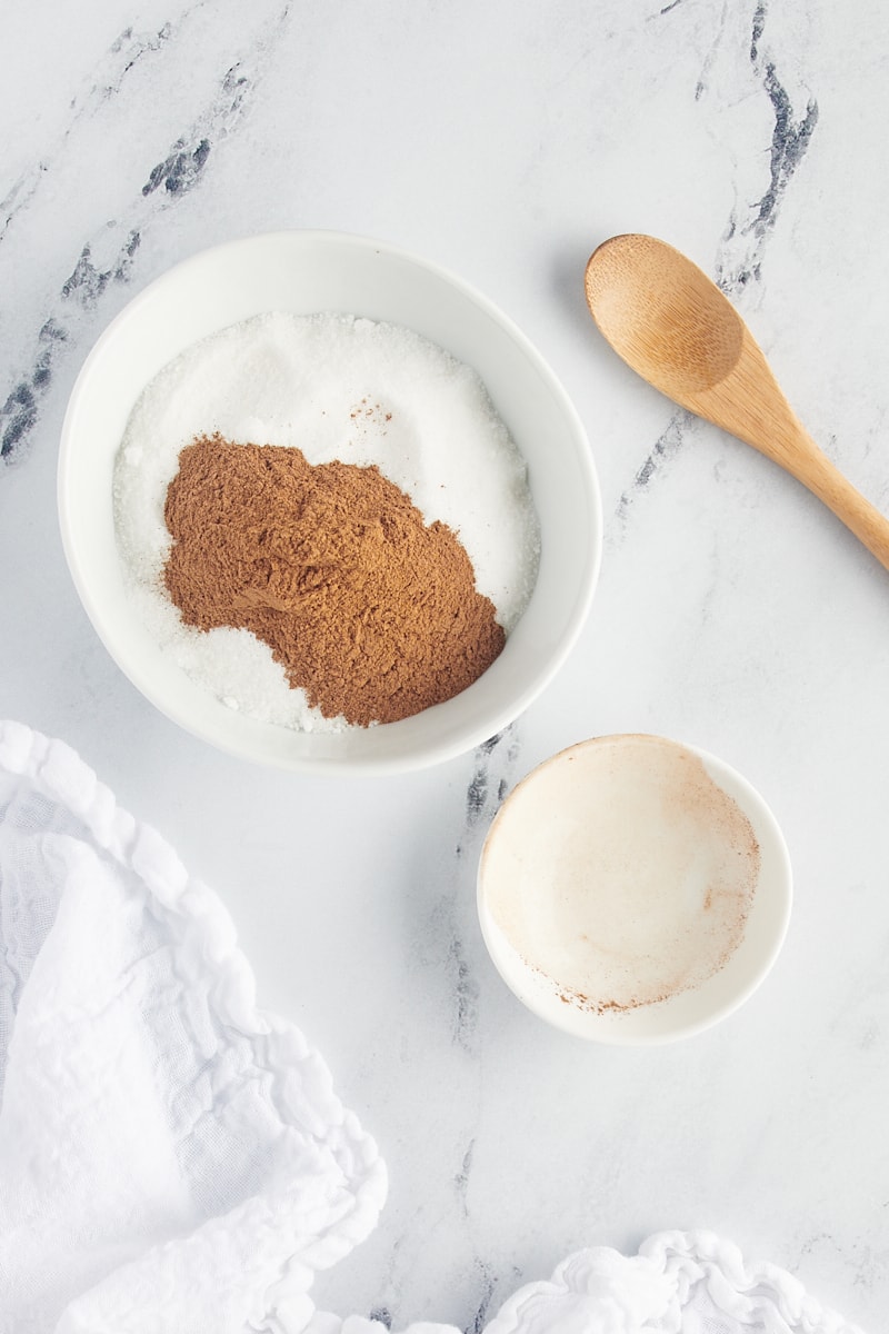 overhead view of cinnamon added to sugar in a white bowl