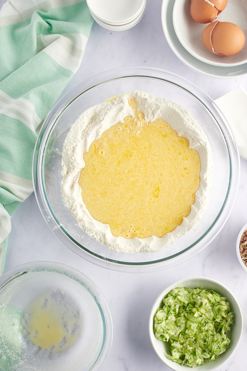 overhead view of wet ingredients added to the well in the center of dry ingredients in a glass mixing bowl