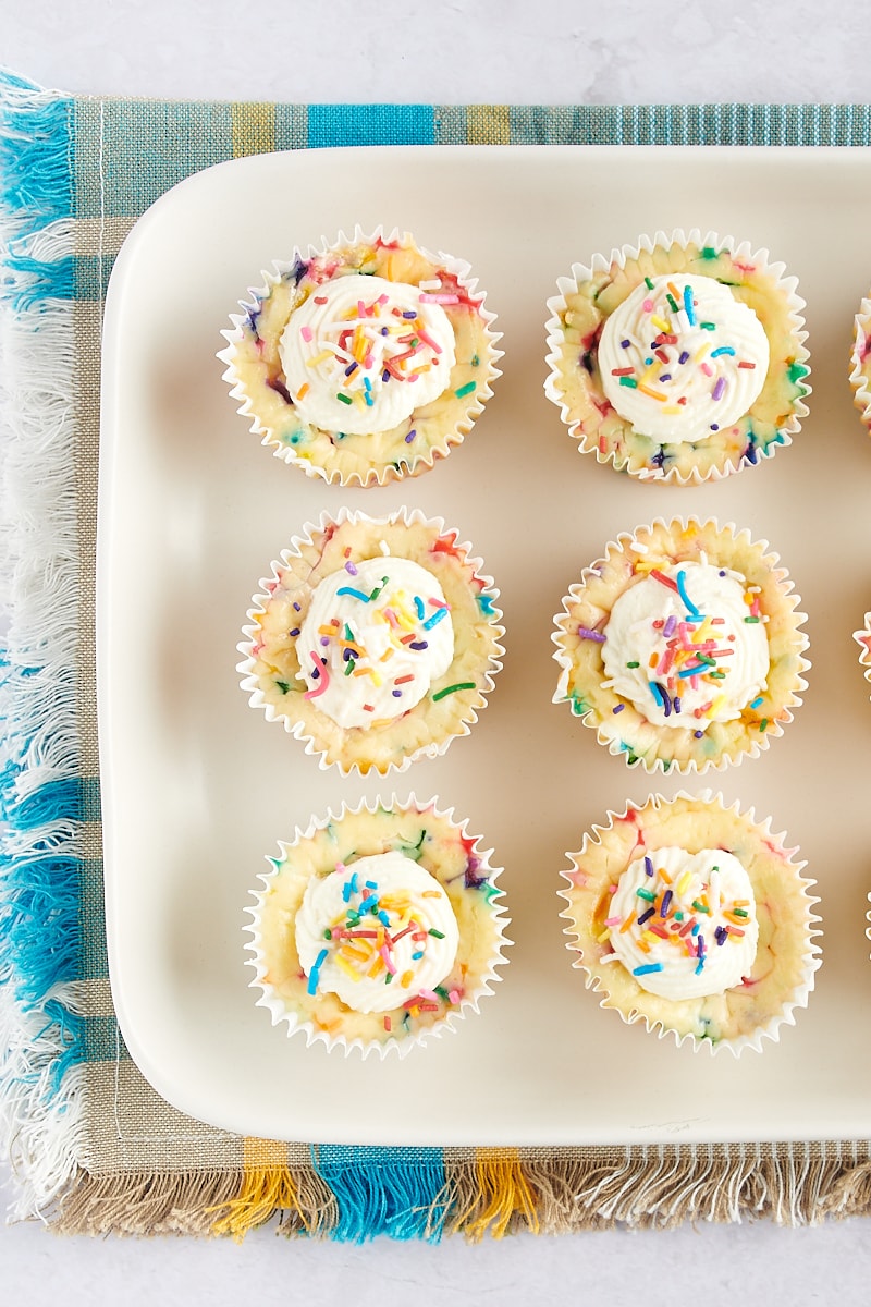 overhead view of Mini Funfetti Cheesecakes on a white tray with a colorful fabric underneath