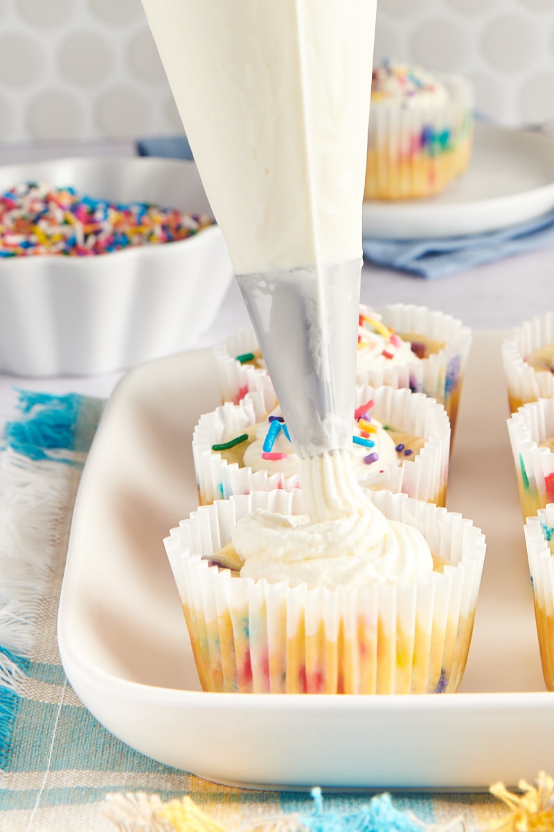 whipped cream being piped onto a Mini Funfetti Cheesecake