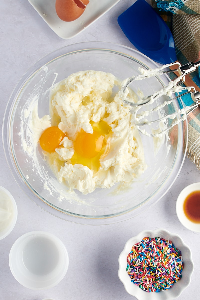 overhead view of eggs added to cheesecake batter in a glass mixing bowl