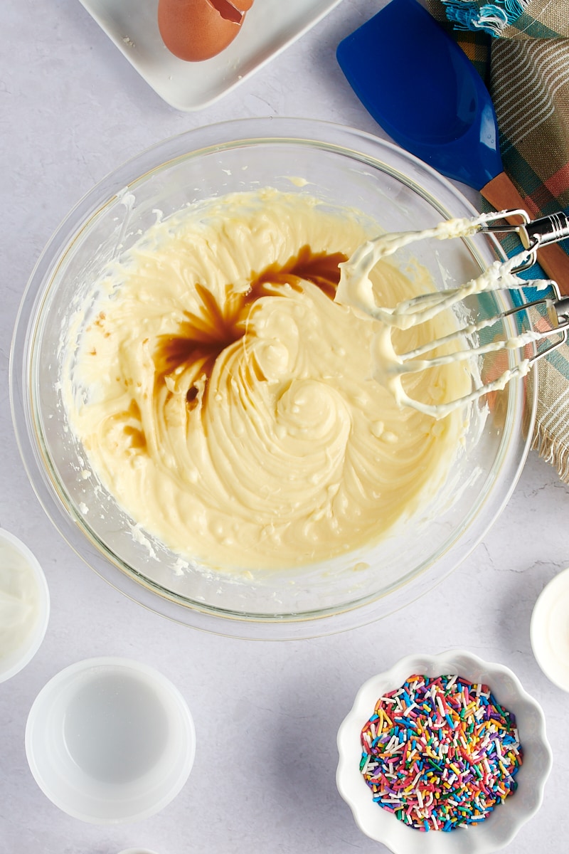 overhead view of vanilla added to cheesecake batter in a glass mixing bowl