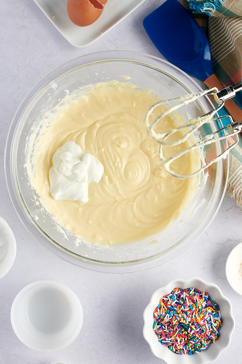 overhead view of sour cream added to cheesecake batter in a glass mixing bowl