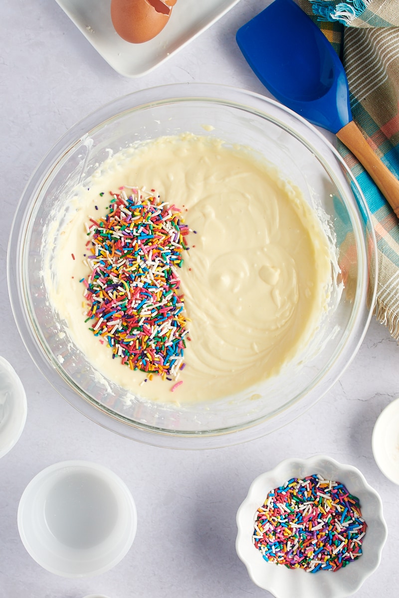 overhead view of sprinkles added to cheesecake batter in a glass mixing bowl