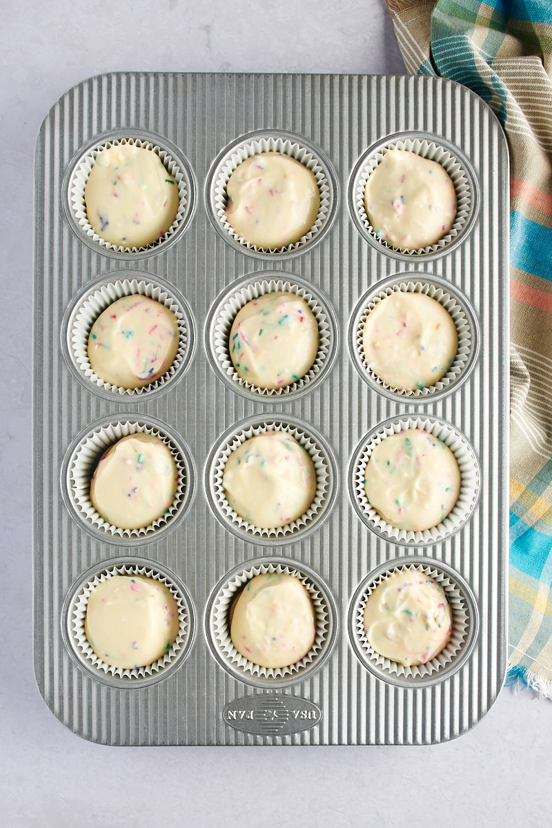 sett ovenfra av Mini Funfetti ostekaker i en muffinsform klar til å gå i ovnen