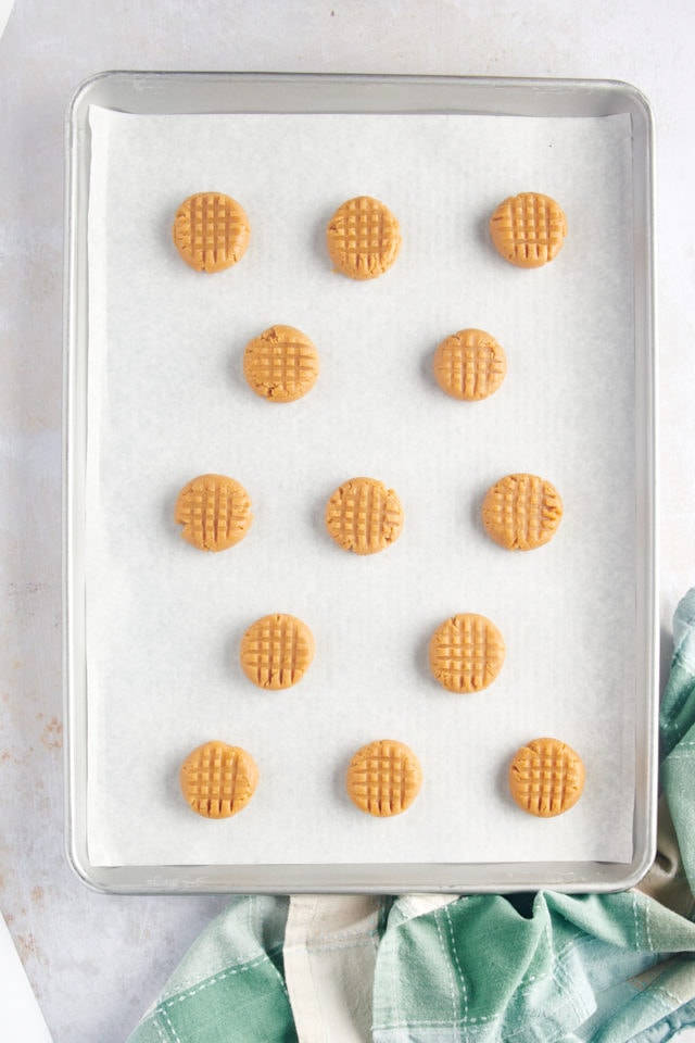 overhead view of a lined baking sheet filled with peanut butter cookie dough with cross-hatch marks