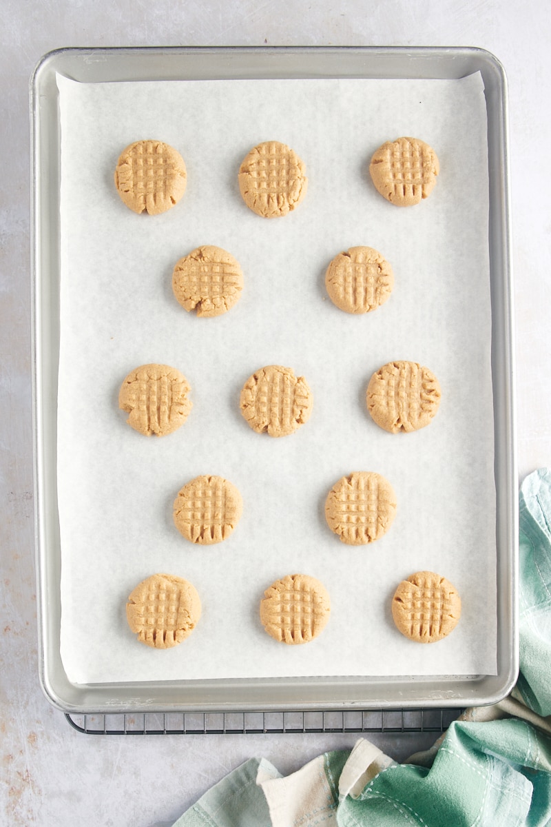 visão aérea de biscoitos de manteiga de amendoim com 3 ingredientes recém-assados ​​em uma assadeira forrada de pergaminho