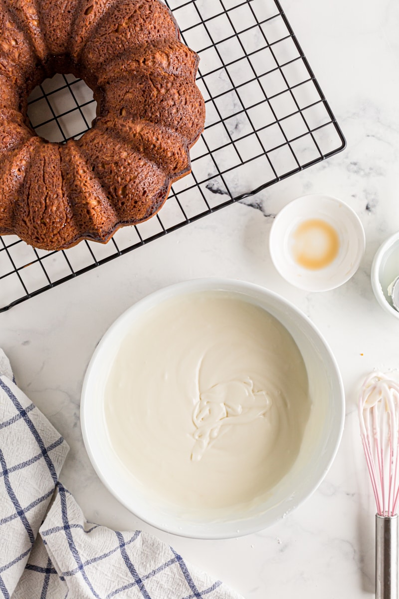 A bowl of glaze next to a cinnamon Bundt cake fresh out of the oven.