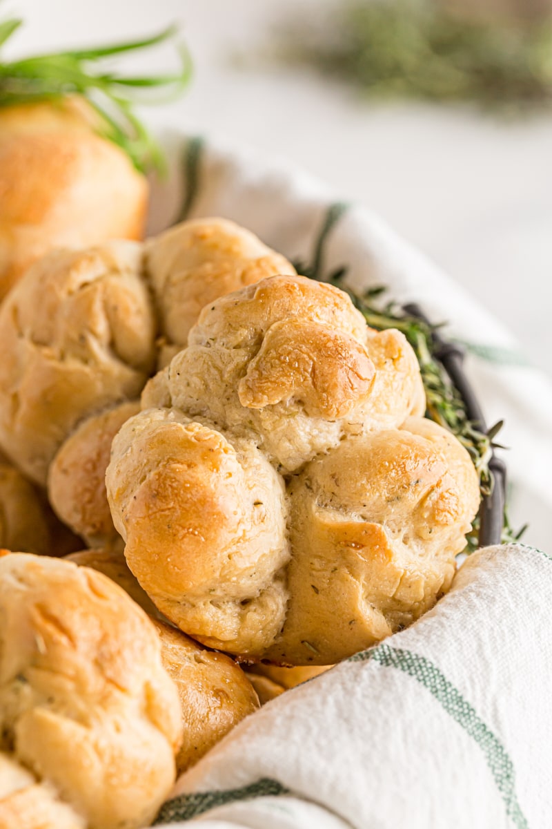 A basket of Herb Cloverleaf Rolls with a sprig of rosemary.