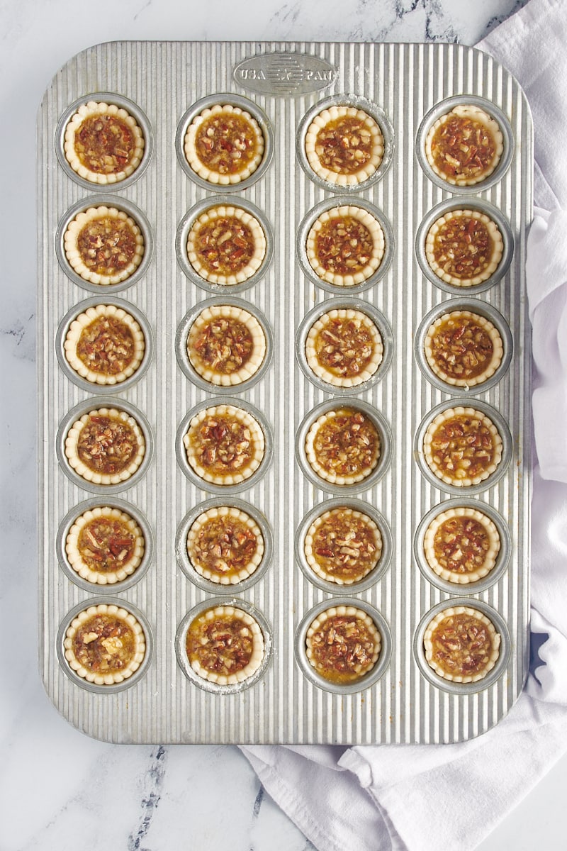 A muffin tin full of pecan mini pies before being baked.