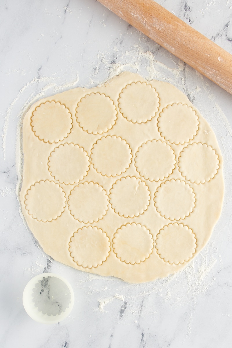 Small circles of pie crust being cut out of a larger crust.