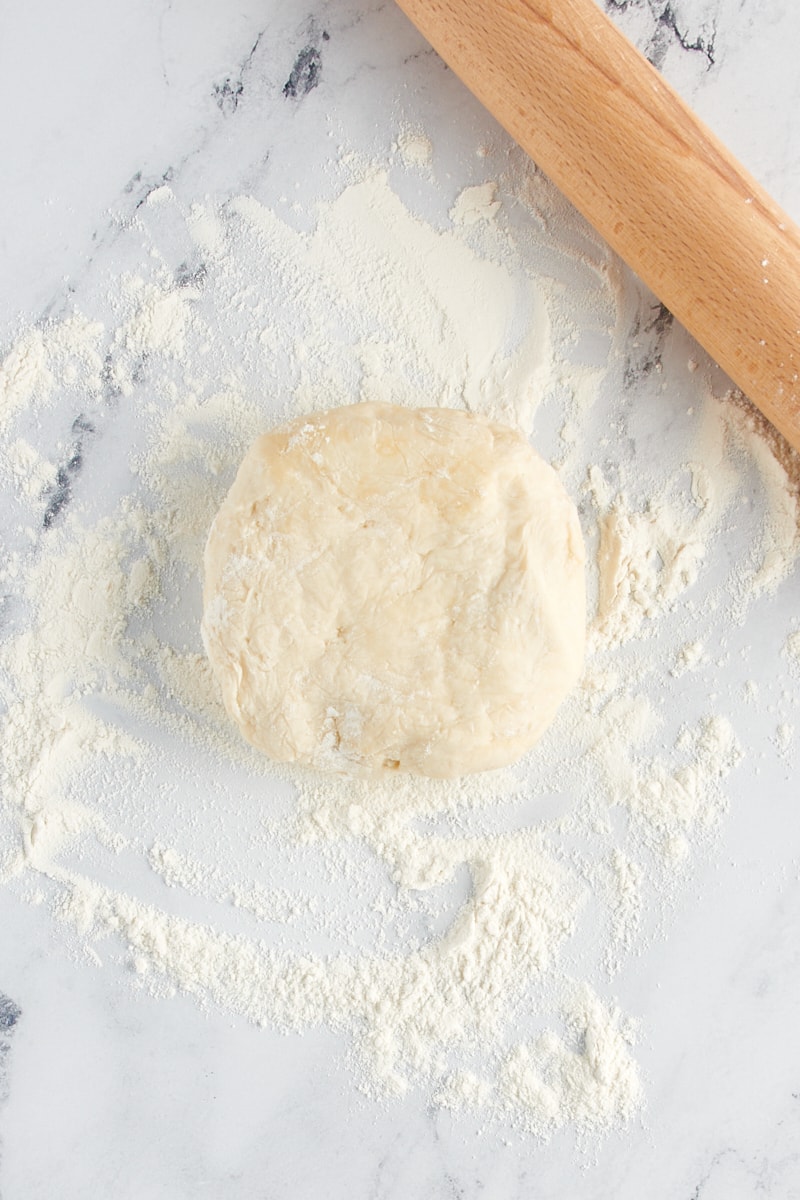 A ball of dough on a counter sprinkled with flour next to a rolling pin.