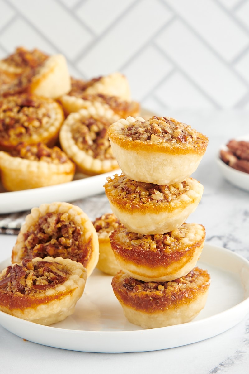 A stack of four mini pies on a plate next to two other mini pies.