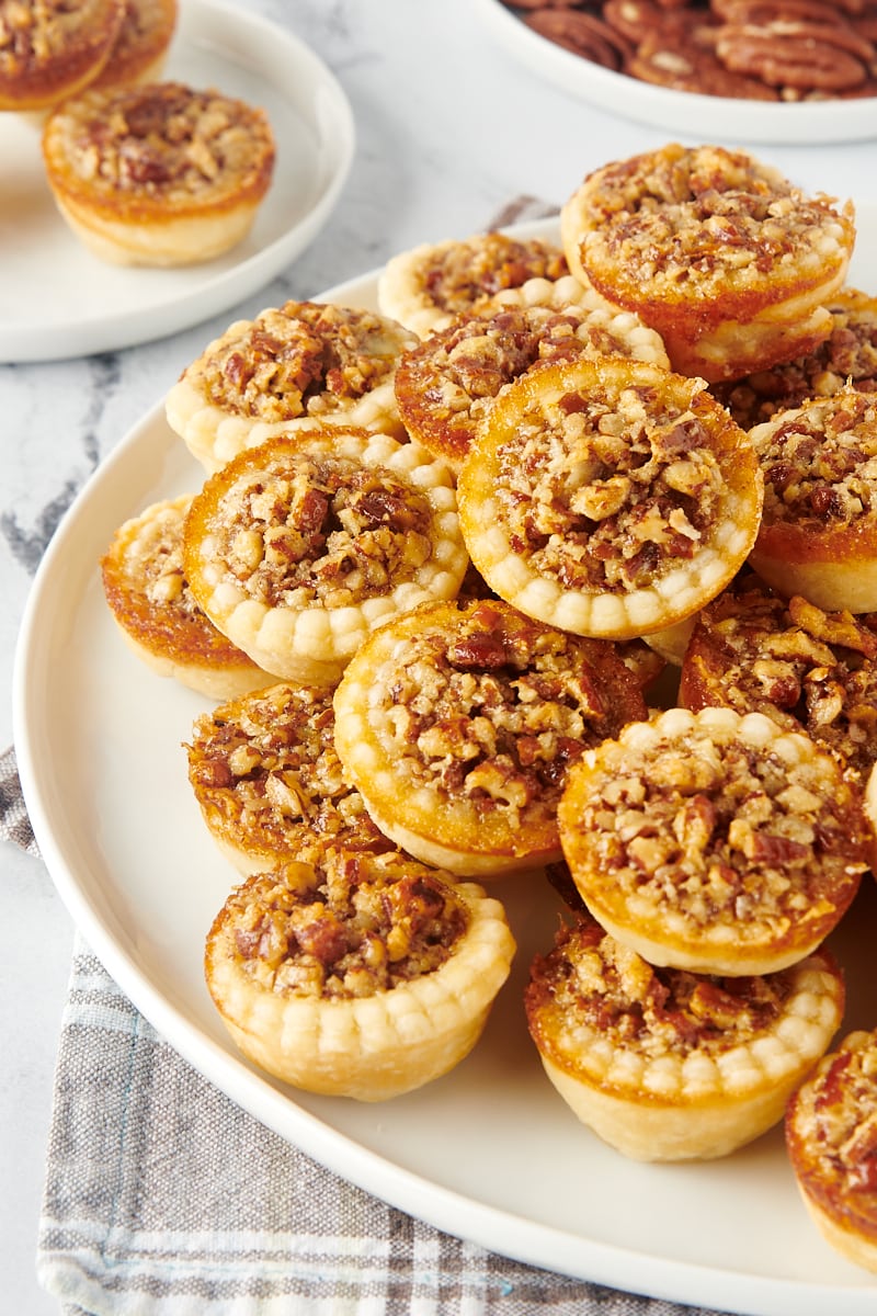 A platter of pecan mini pies with a plated mini pie in the background.