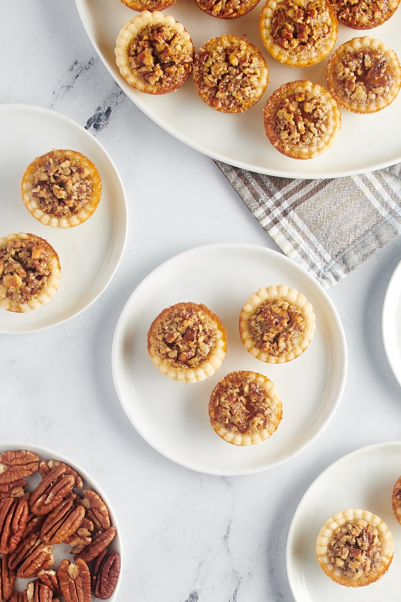 Three pecan mini pies on a plate next to a platter with the rest of the pies.