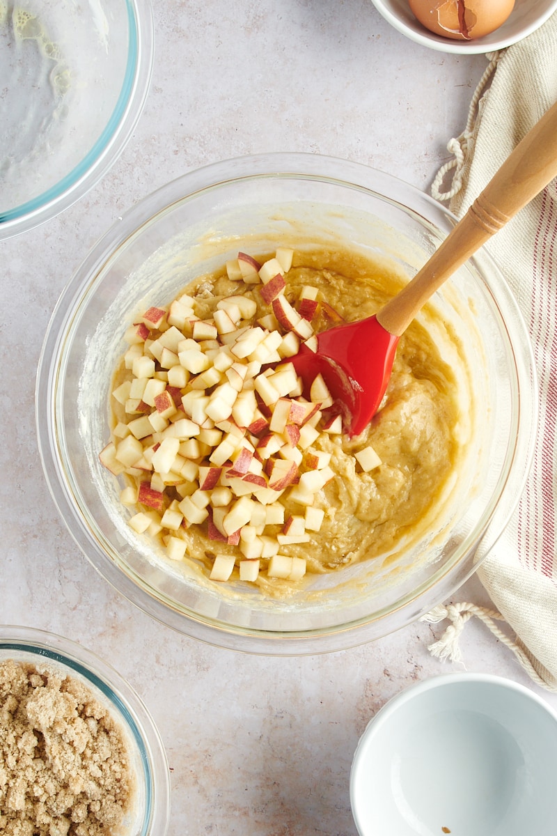 overhead view of apples added to muffin batter in a glass mixing bowl