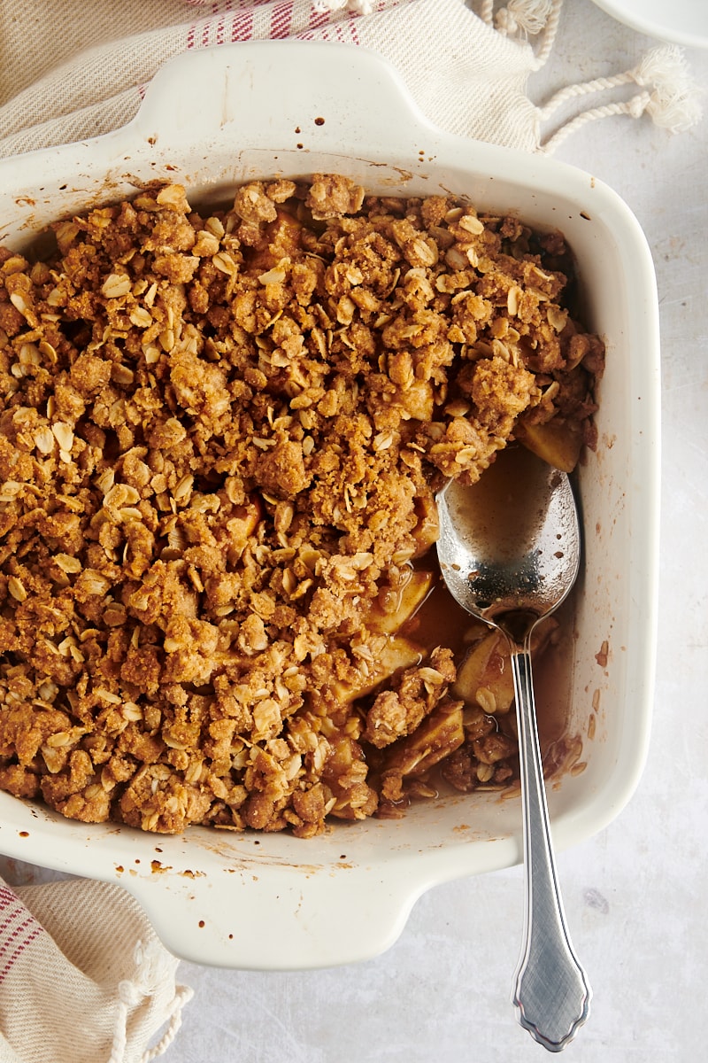 A portion of Apple Crisp missing from the pan with a spoon in the empty space.