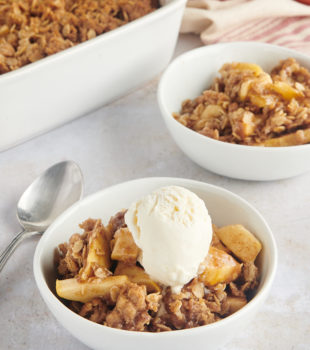 A bowl full of cooked apples and streusel with a scoop of ice cream on top.