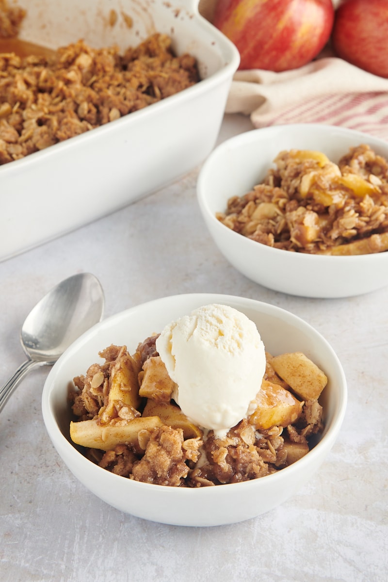 A bowl full of cooked apples and streusel with a scoop of ice cream on top.