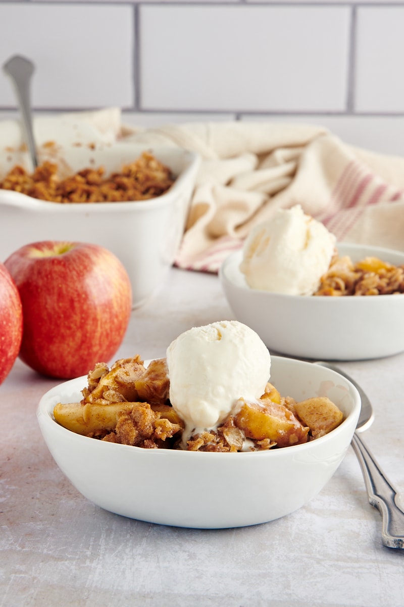 A side view of a single bowl of apple crisp with ice cream.