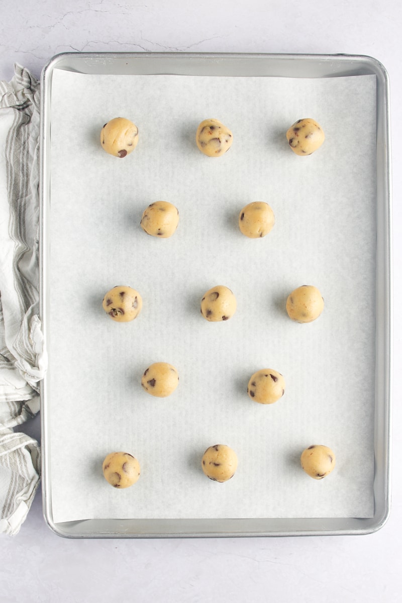 Balls of chocolate chip cookie dough spread out on a baking sheet.