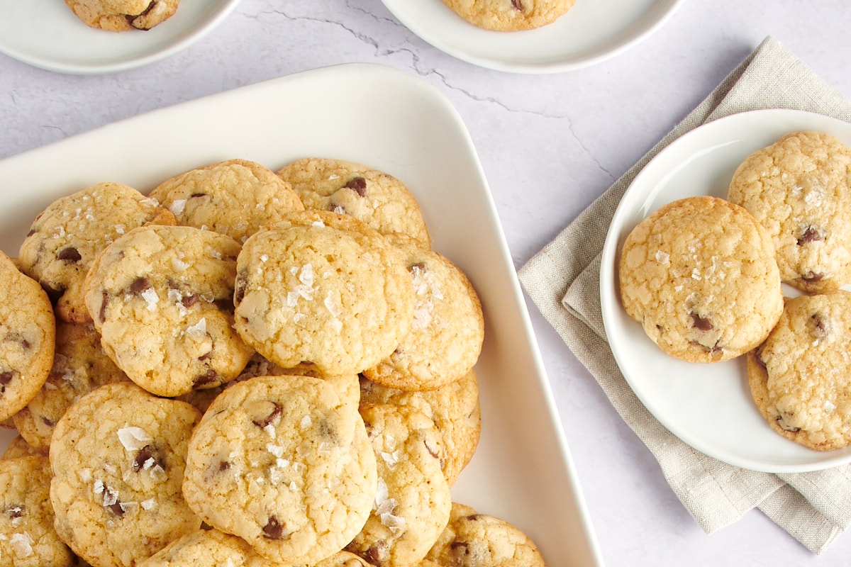 Three cookies on a plate next to a platter piled with more cookies.