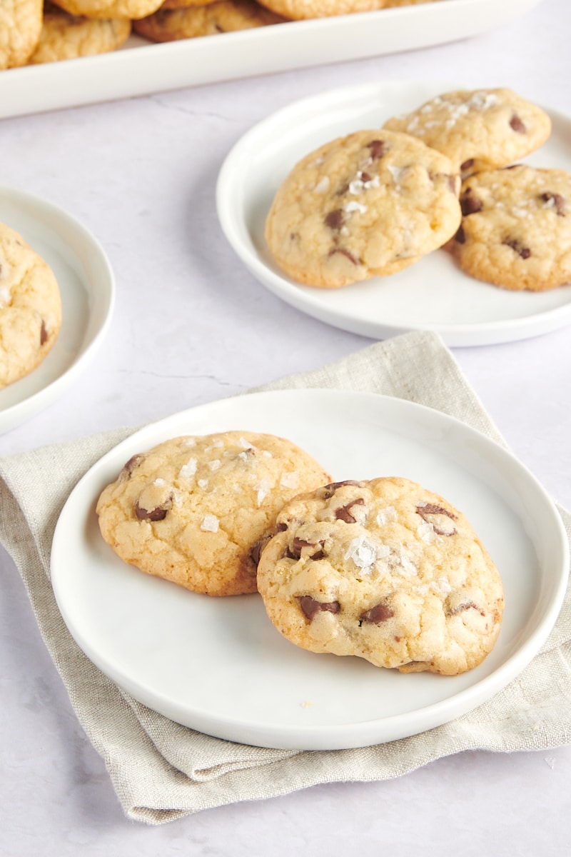 Two salted chocolate chip cookies on a plate with a plate of three cookies in the background.