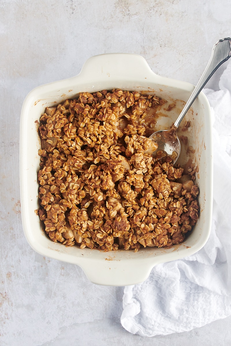 overhead view of Brown Butter Pear Crisp in a white baking dish with a serving spoon in one corner