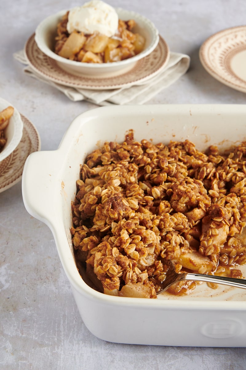 Brown Butter Pear Crisp in a white baking dish with servings in bowls in the background