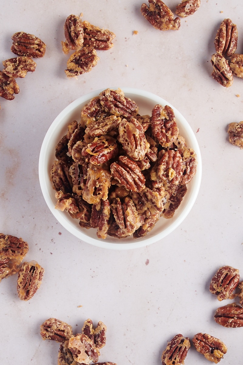 overhead view of Glazed Pecans in a white bowl with more pecans scattered around it