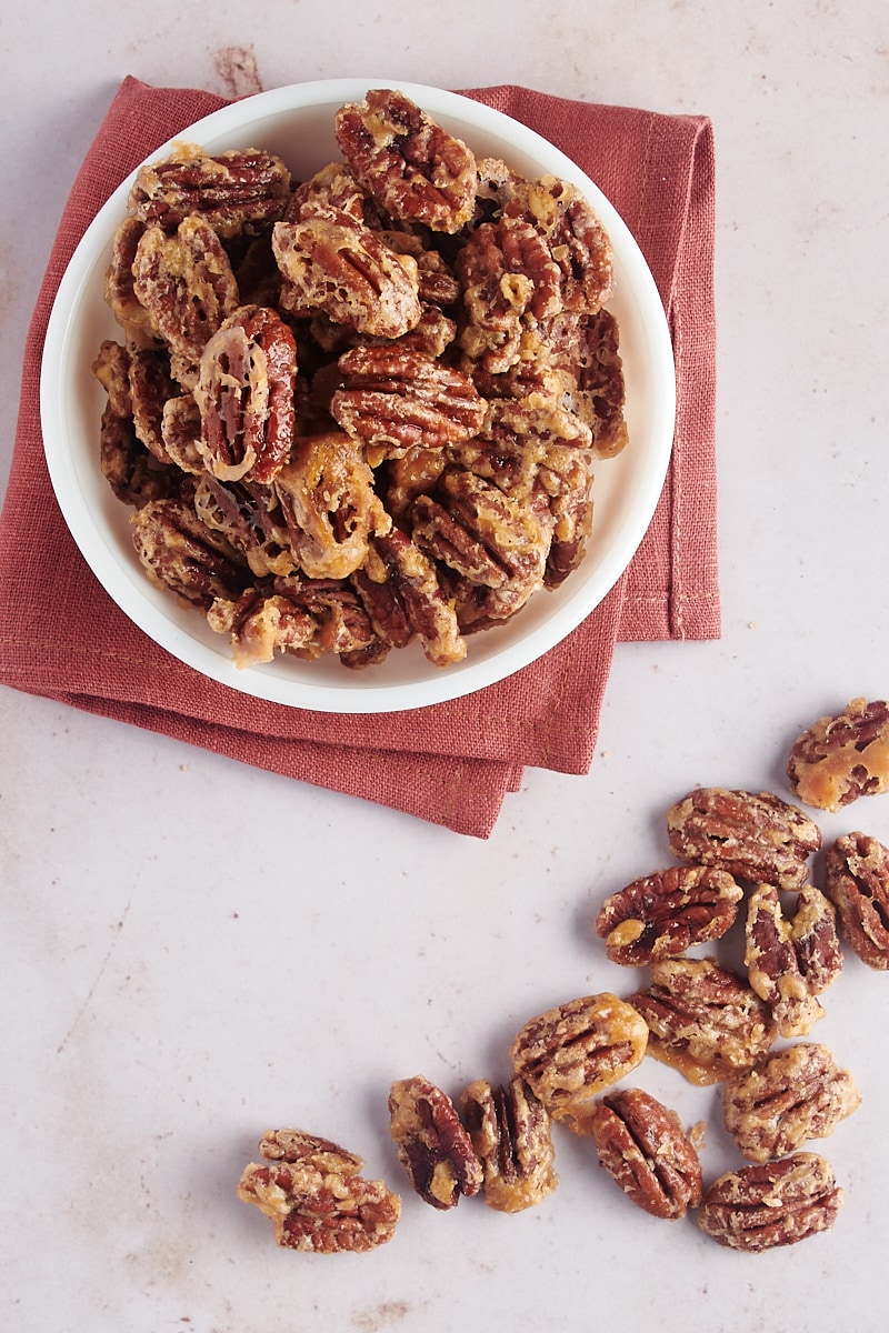 overhead view of Glazed Pecans in a white bowl with more pecans beside the bowl