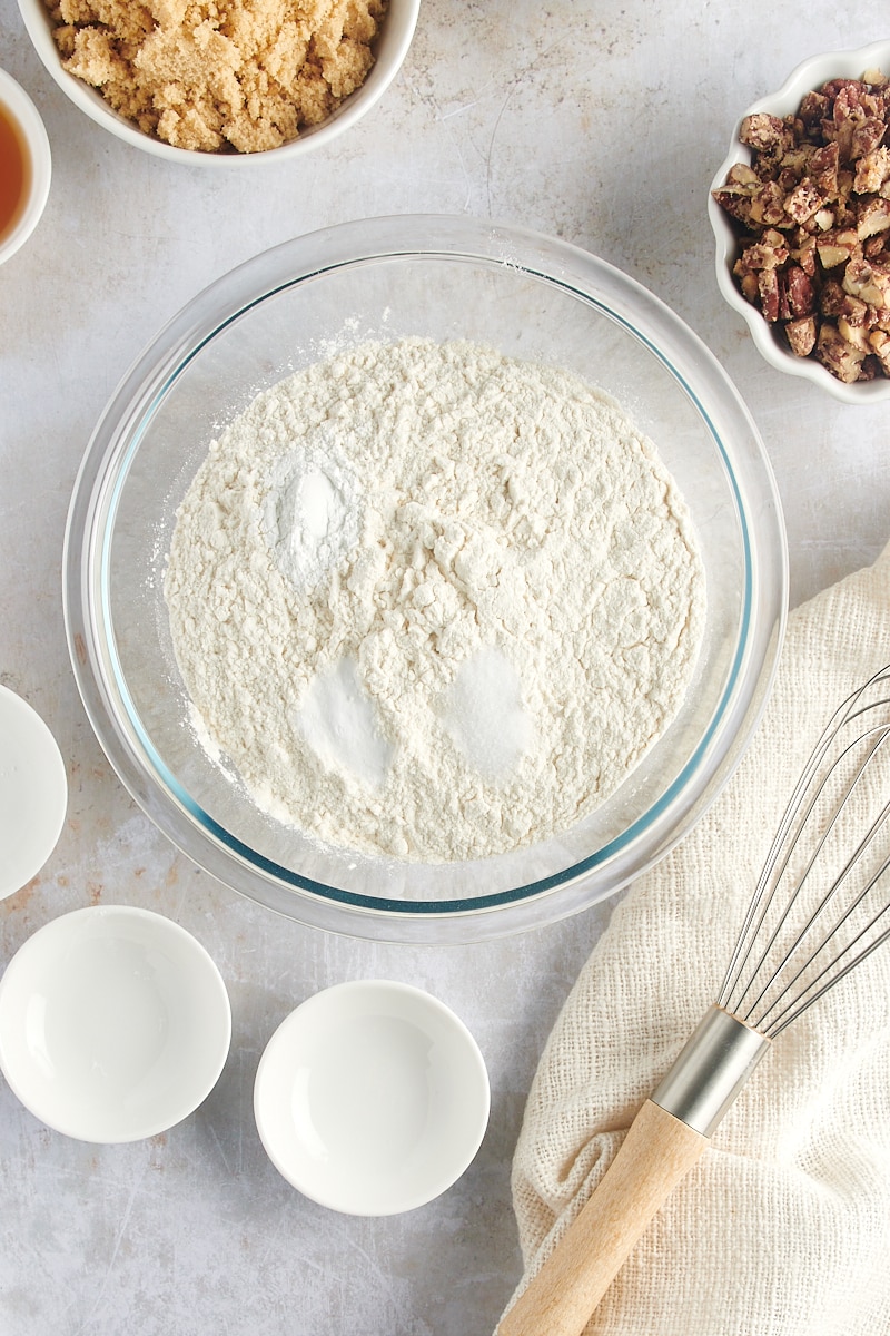 overhead view of flour, baking powder, baking soda, and salt in a glass mixing bowl