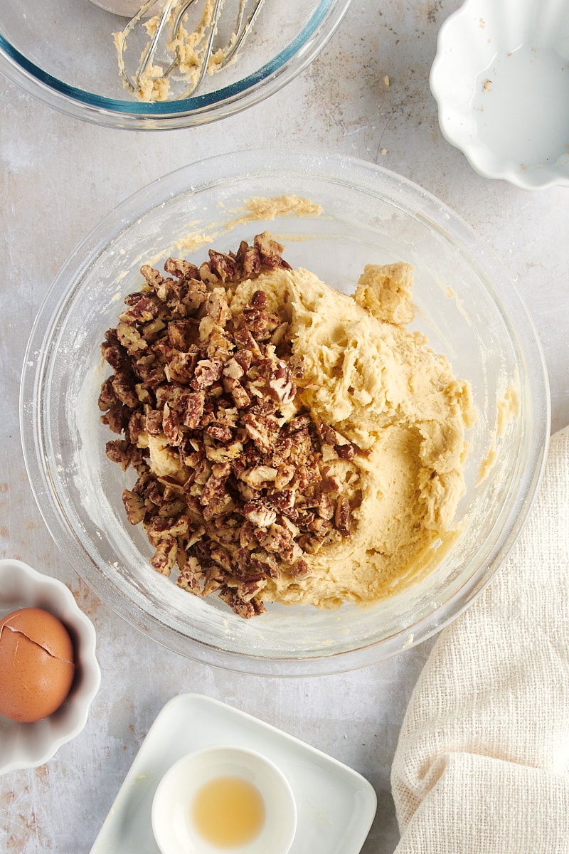 overhead view of chopped pecans added to cookie dough in a glass mixing bowl