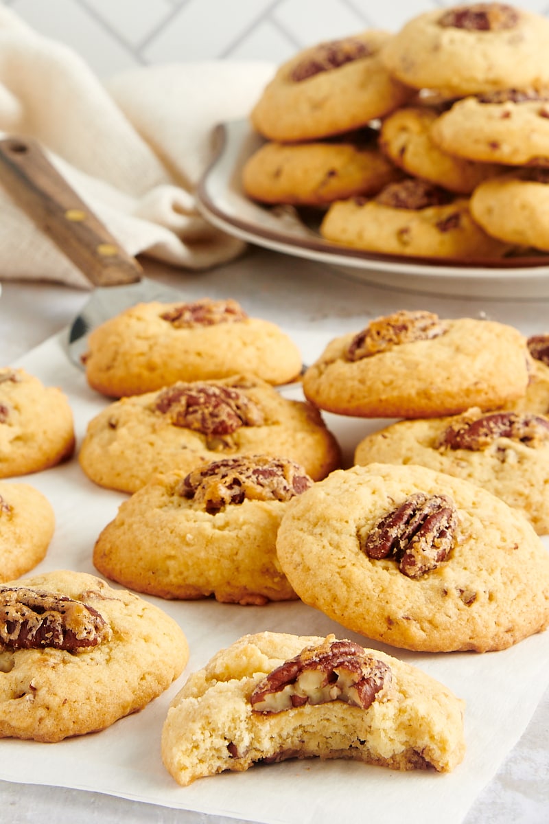 Maple Pecan Cookies på pergamentpapir med en tallerken med flere småkager i baggrunden