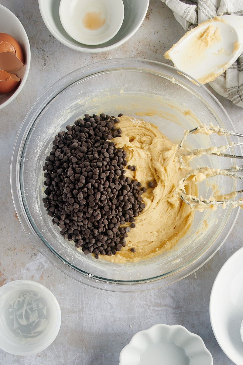overhead view of chocolate chips added to cake batter in a glass mixing bowl