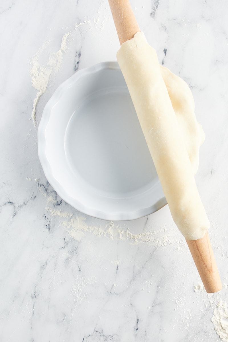 overhead view of pie crust dough on a rolling pin on top of a pie plate