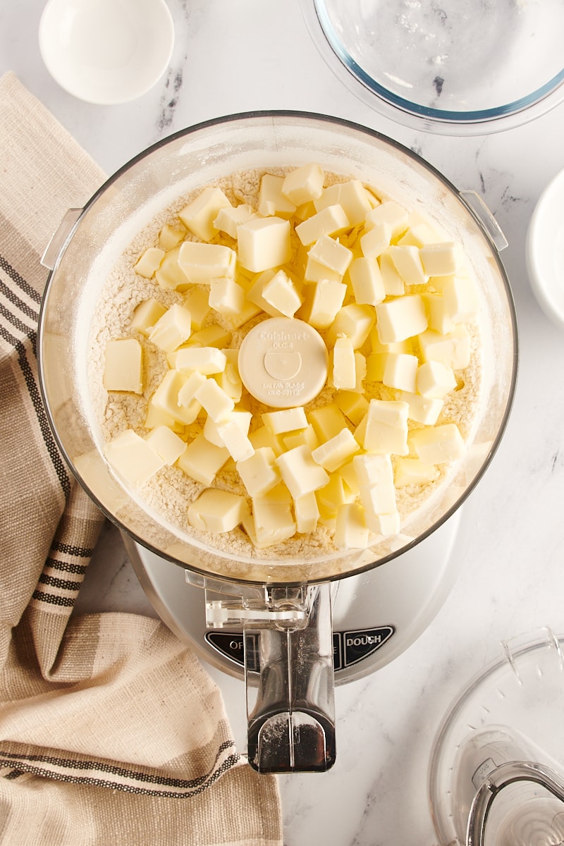 overhead view of butter added to pie crust ingredients in a food processor