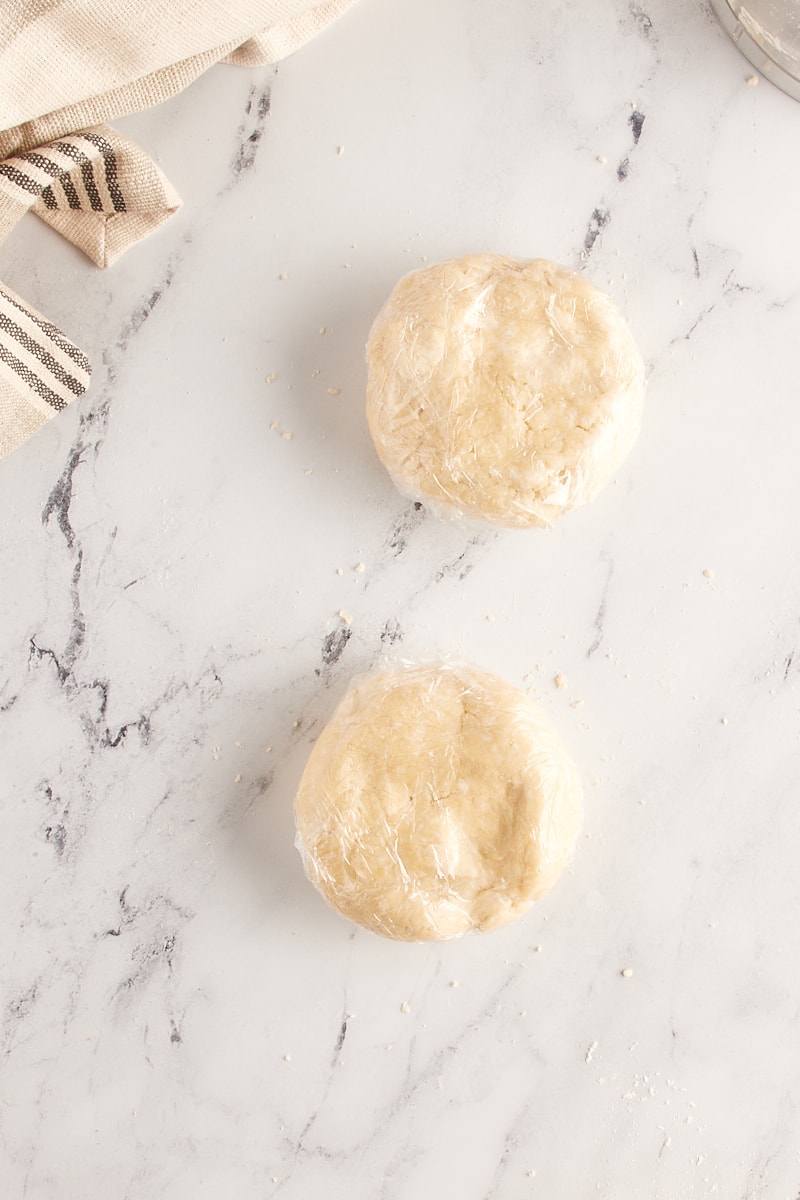 overhead view of two discs of pie crust dough wrapped in plastic wrap