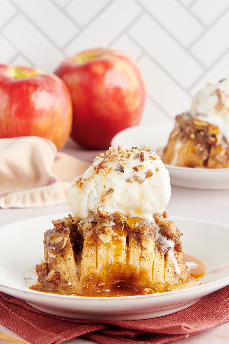 a baked hasselback apple topped with ice cream, caramel sauce, and nuts