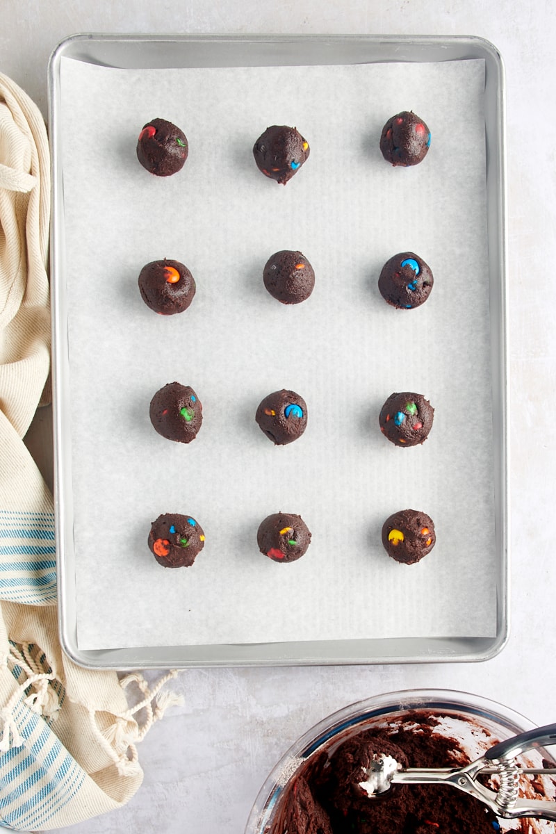 overhead view of portioned Chocolate M&M Cookie dough on a parchment-lined baking sheet