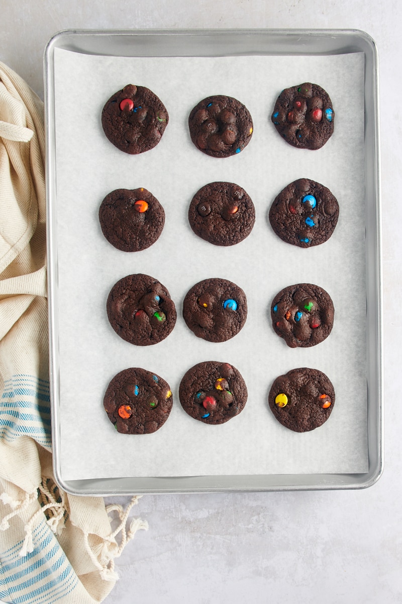 overhead view of freshly baked Chocolate M&M Cookies on a parchment-lined baking sheet on a wire rack