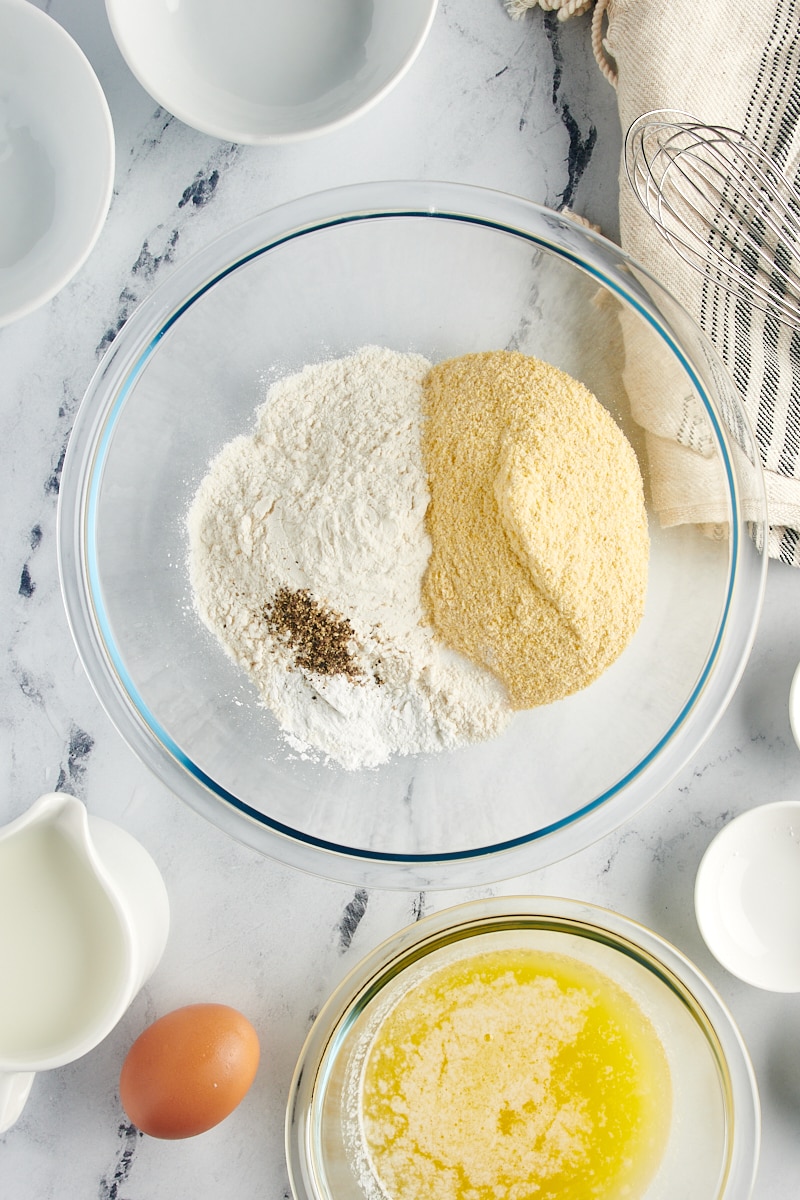 Dry and wet ingredients for corn muffins in glass mixing bowls.