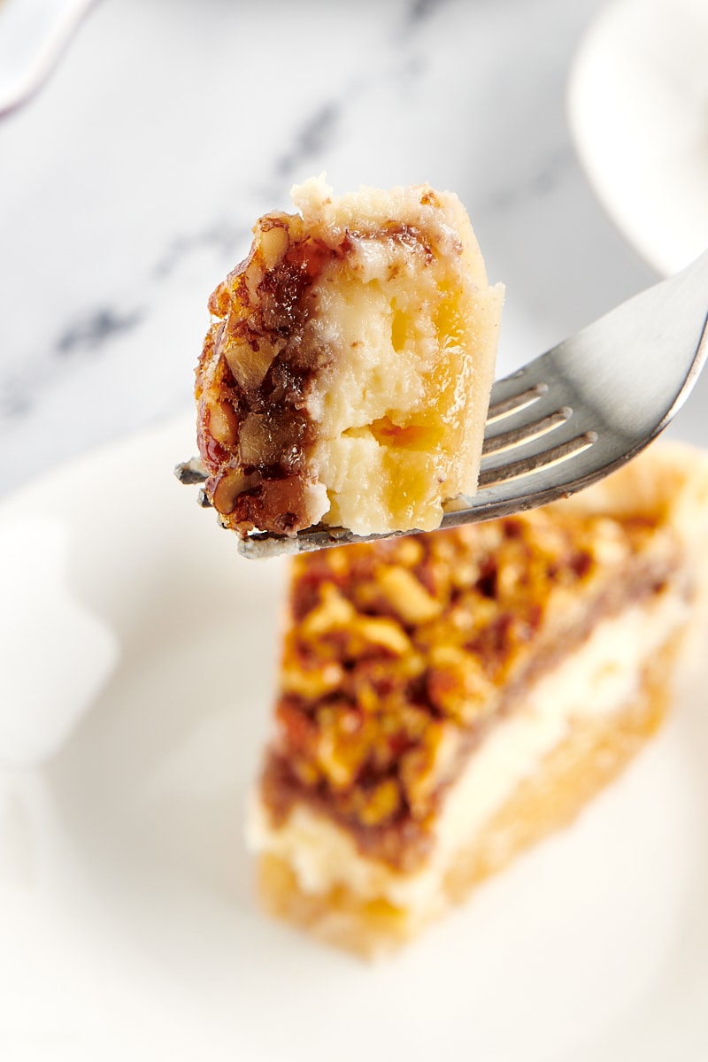 a forkful of Pecan Cheesecake Pie with remaining slice of pie in the background
